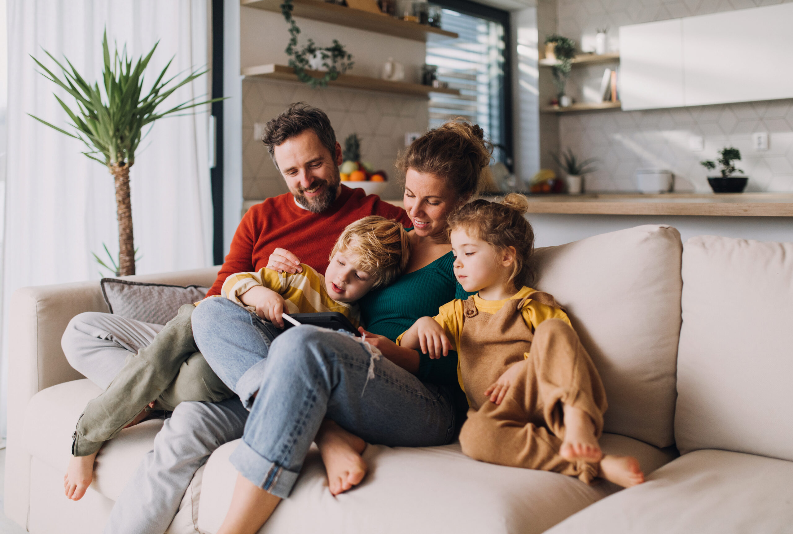Stock image of a family sitting on the couch together looking at a tablet